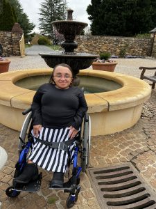 Vilissa in a wheel chair in front of a water fountain