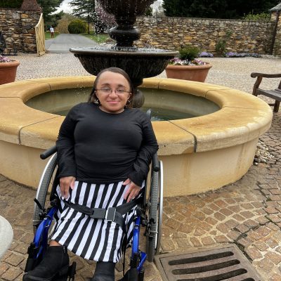 Vilissa in a wheel chair in front of a water fountain