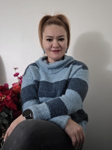 Aleida sitting with arms crossed in front of a wall with folower to the side