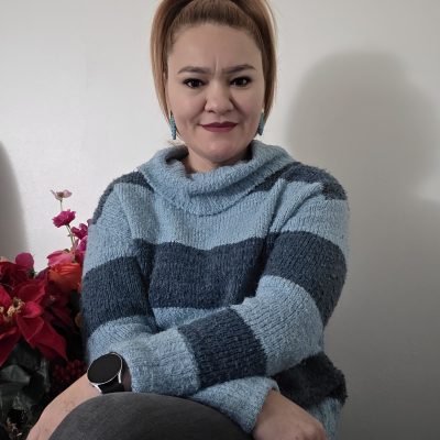 Aleida sitting with arms crossed in front of a wall with folower to the side