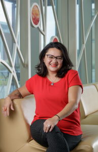 Mariela seated on a couch in front of windows.