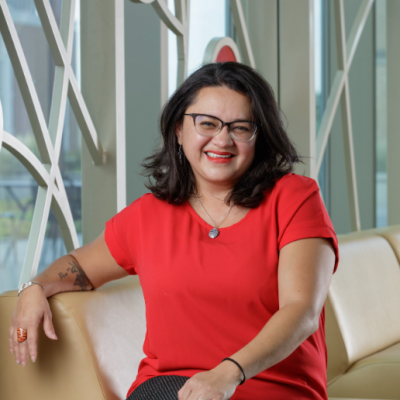 Mariela seated on a couch in front of windows.