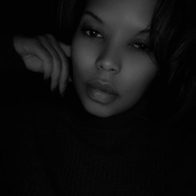 Headshot of April in a dark background with a hand on her cheek.