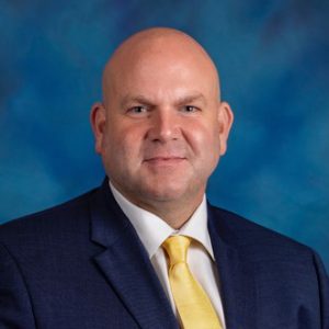 Andrew in front of a blue screen wearing a jacket and tie