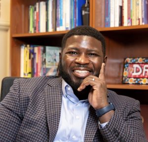 Curtis sitting in front of a bookshelf with his hand on his cheek