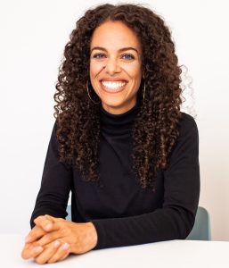 Erika seated at a table with hand folded wearing a black shirt