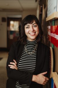 Leslie standing in a hallway with arms crossed.